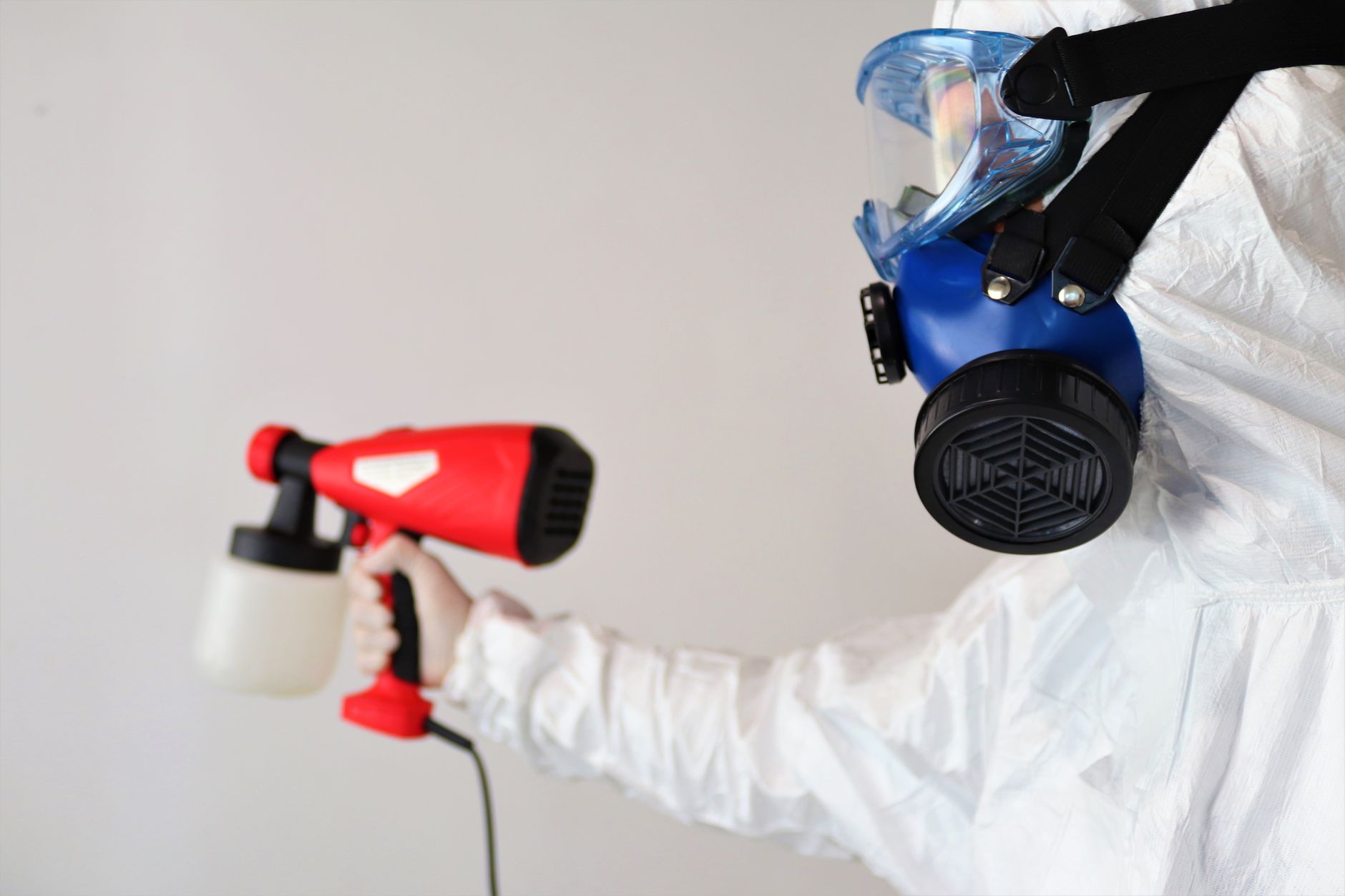 A technician in full PPE inspecting a wall for mold in a dimly lit Indian Creek basement, with specialized equipment visible.